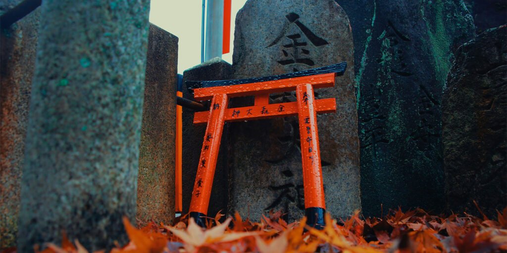 Piccolo torii appoggiato su un muretto con foglie sullo sfondo